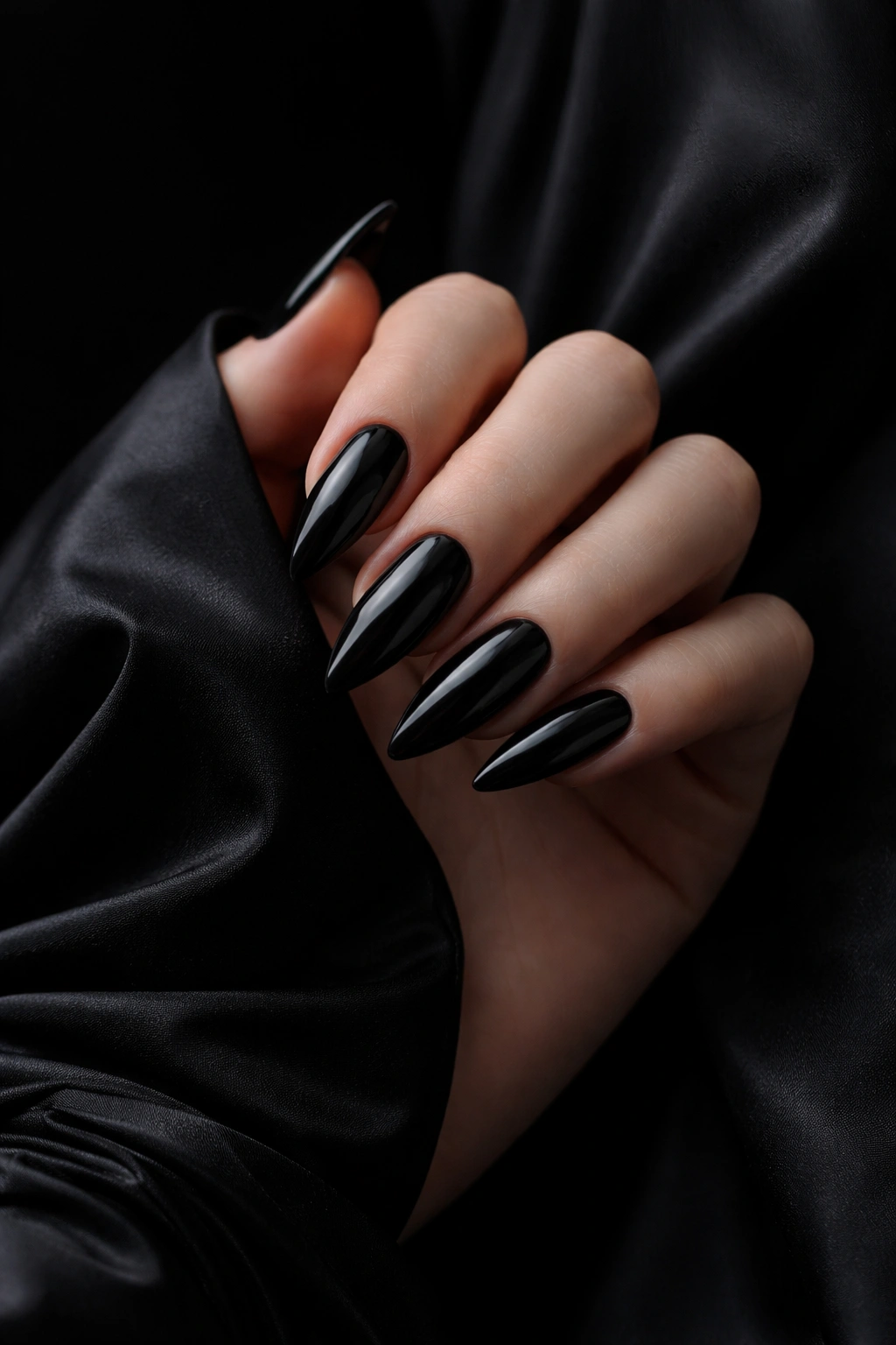 Close-up of black nails with glossy finish against a black dress backdrop