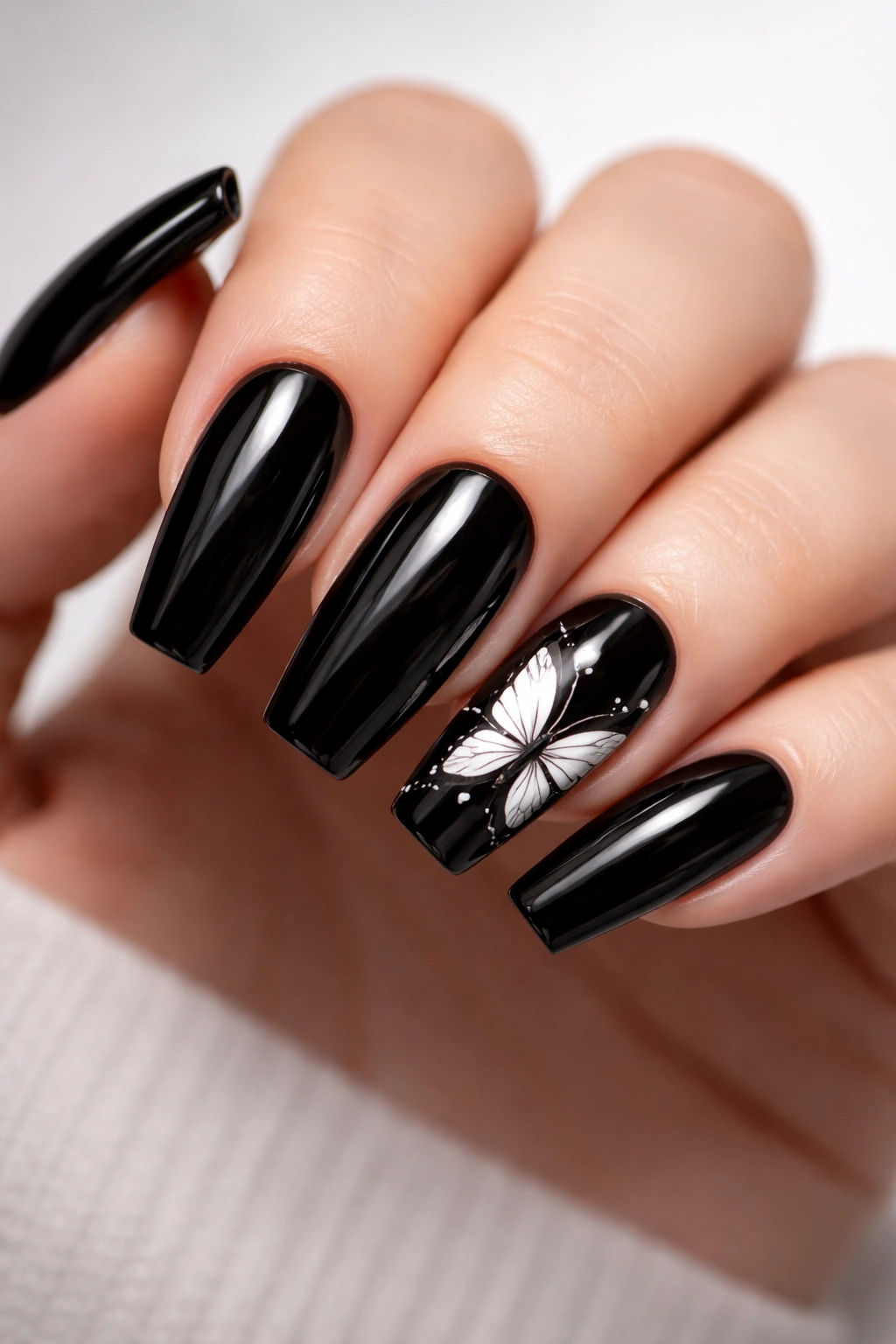 Close-up of black acrylic nails with a white butterfly accent on the ring finger