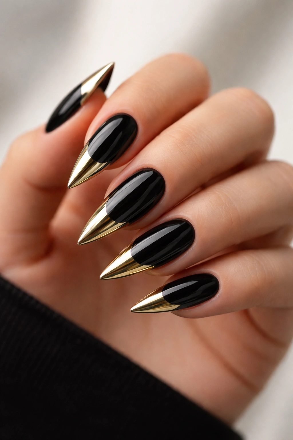 Close-up of black stiletto nails with chrome gold tips reflecting light