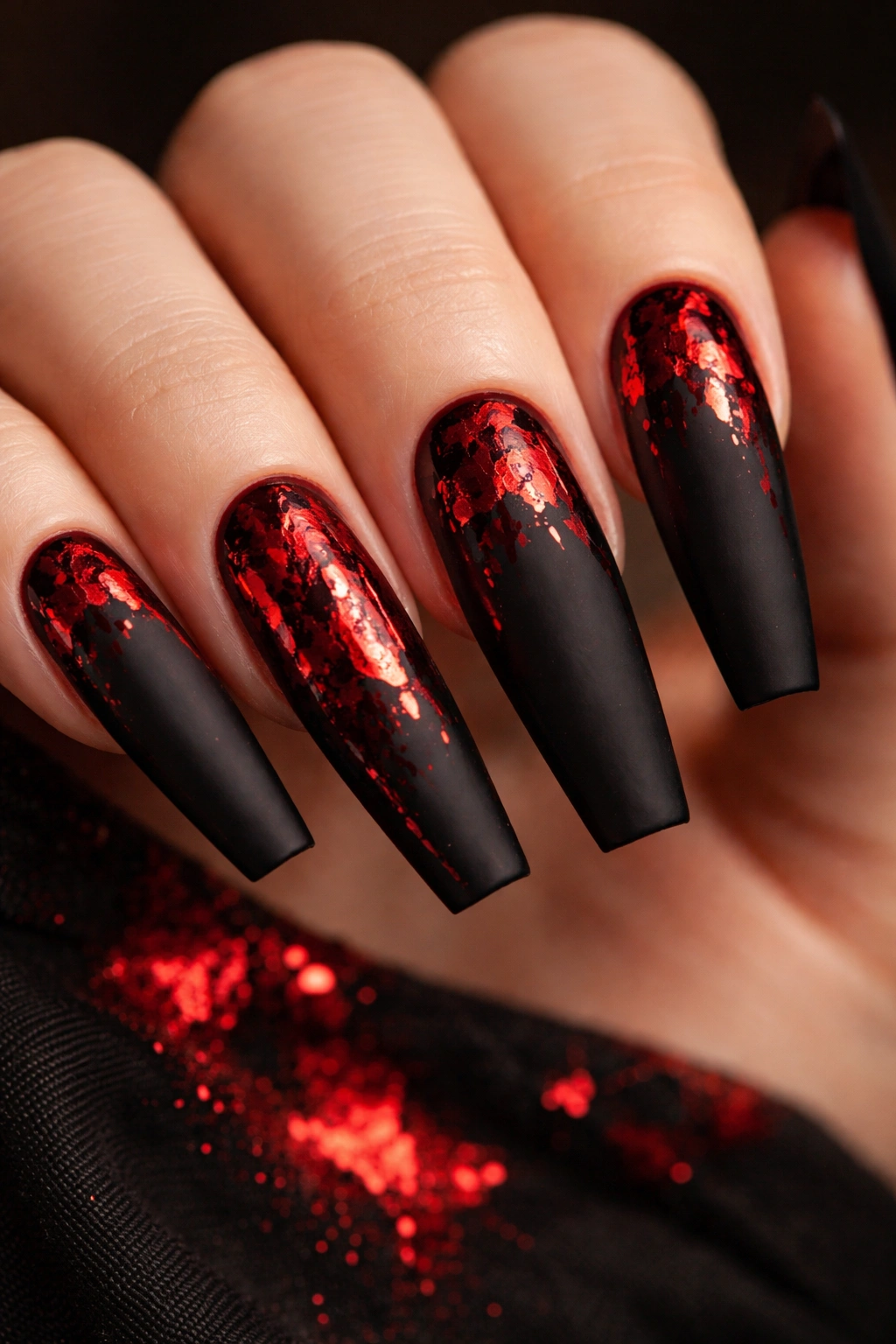 Close-up of matte black coffin nails with red foil accents catching light