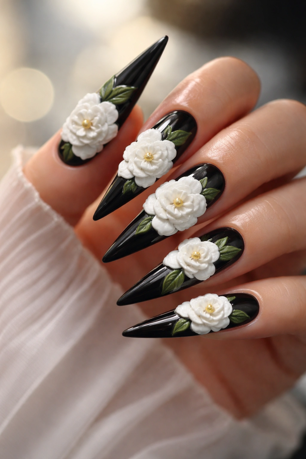 Close-up black stiletto nails with white raised gardenia blooms