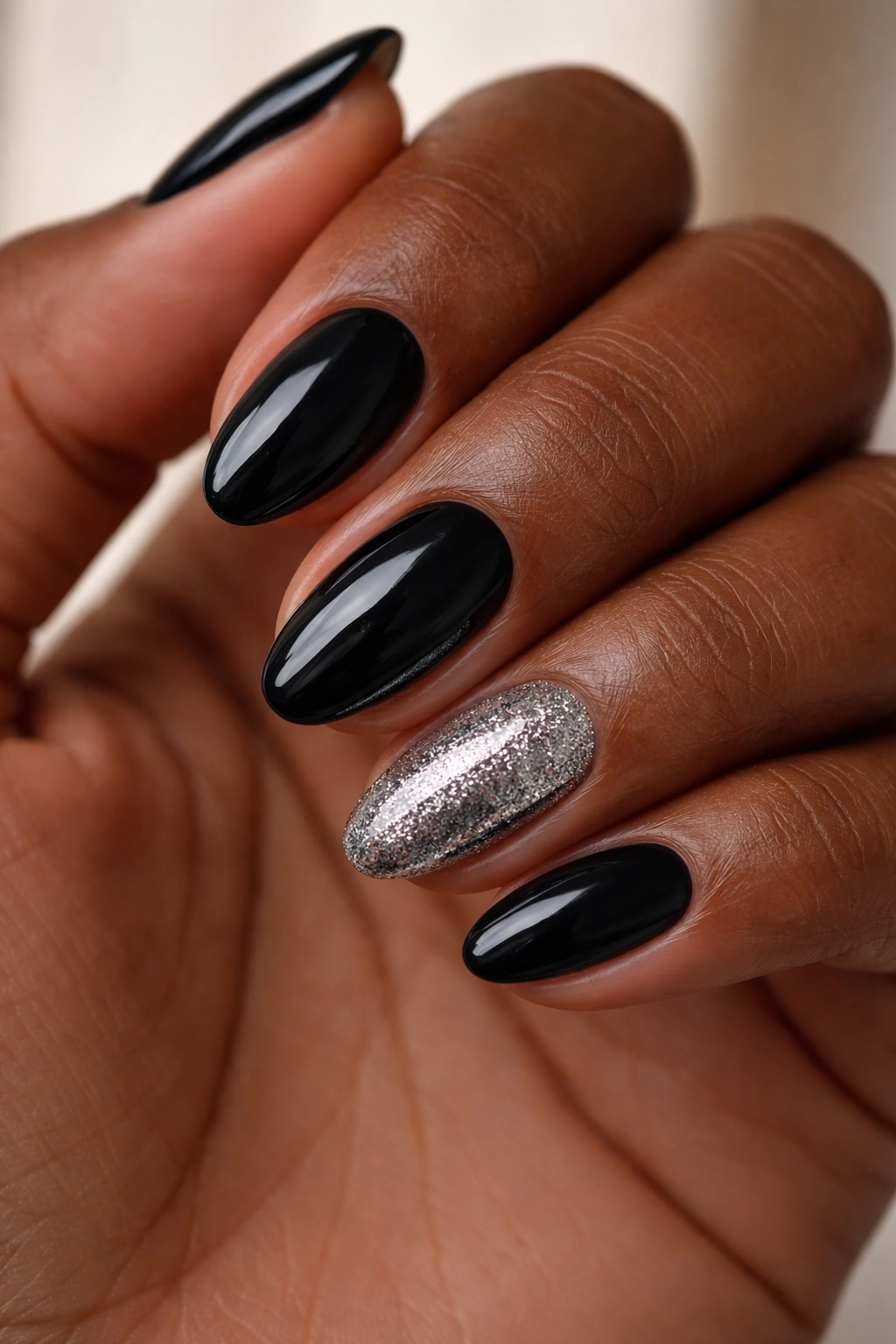 Dark-skinned hand with short almond nails and a single glitter-accent nail