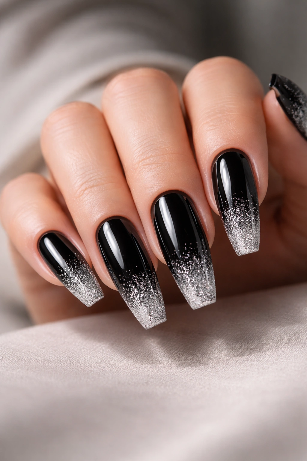 Close-up of coffin nails with glossy black polish and silver glitter ombre at the tips