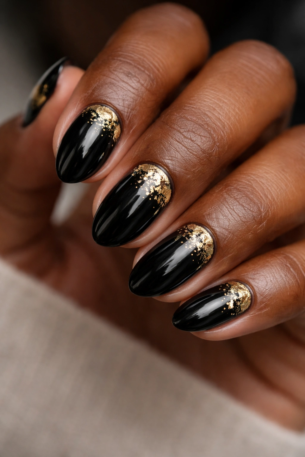 Short almond nails in black with gold foil accents on dark skin