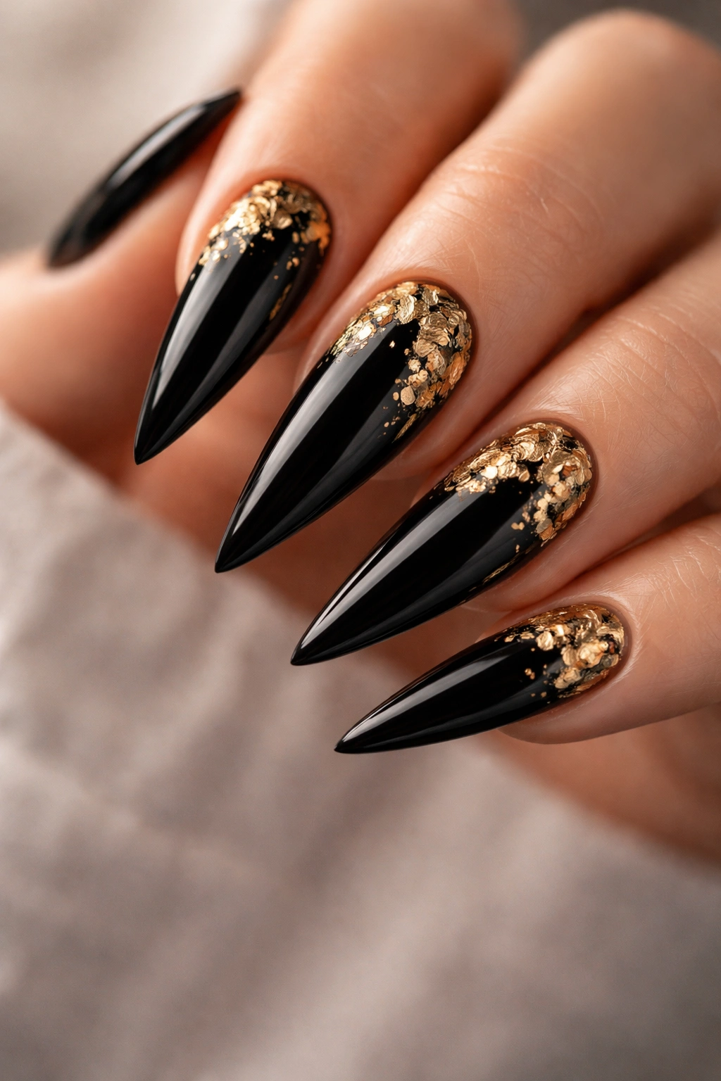 Close-up of glossy black stiletto nails with a small gold leaf accent on one nail