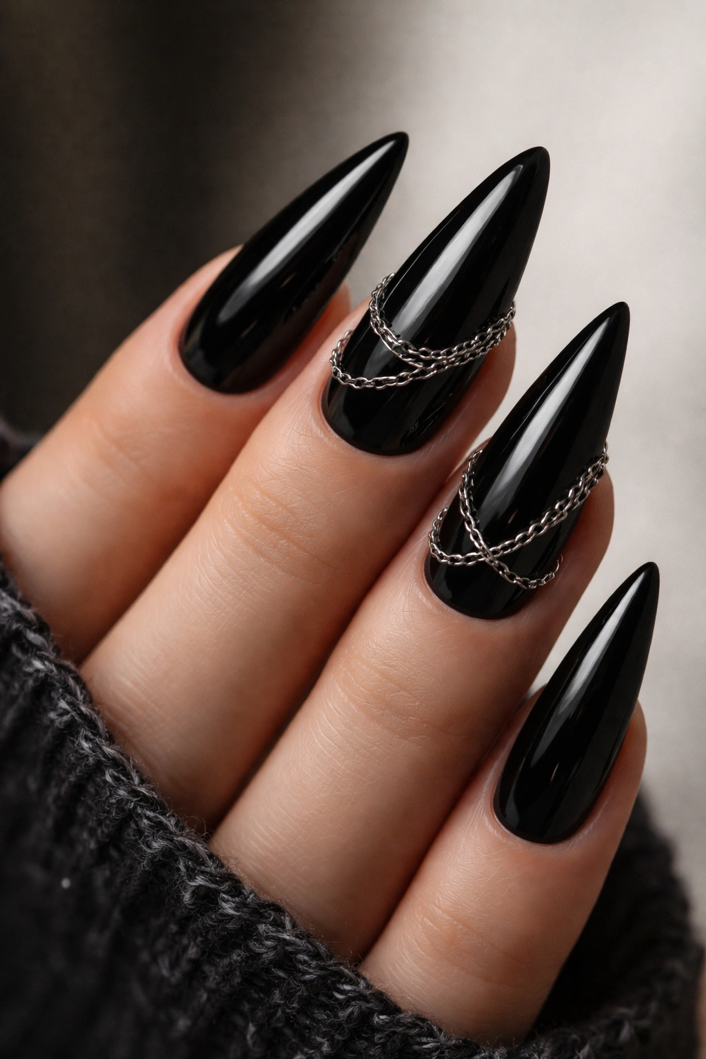 Close-up of glossy black stiletto nails with delicate silver chains draped on the ring and middle fingers.