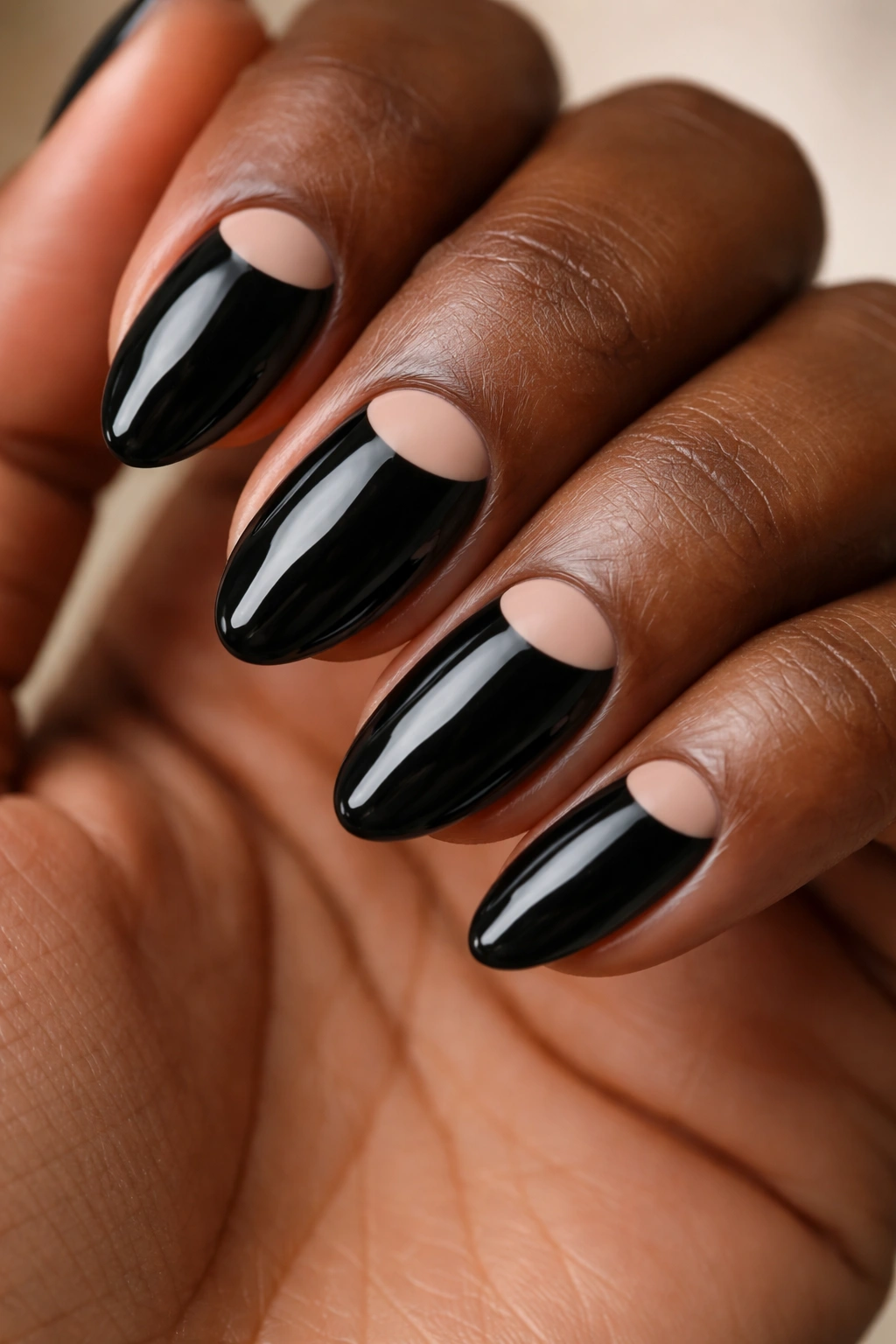 Close-up of black almond nails with nude half-moon cutouts near the cuticle