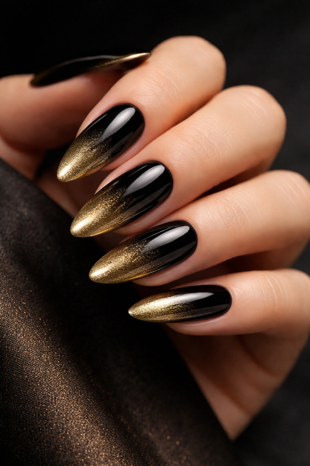 Long oval nails in a black to gold ombre with reflective gold tips