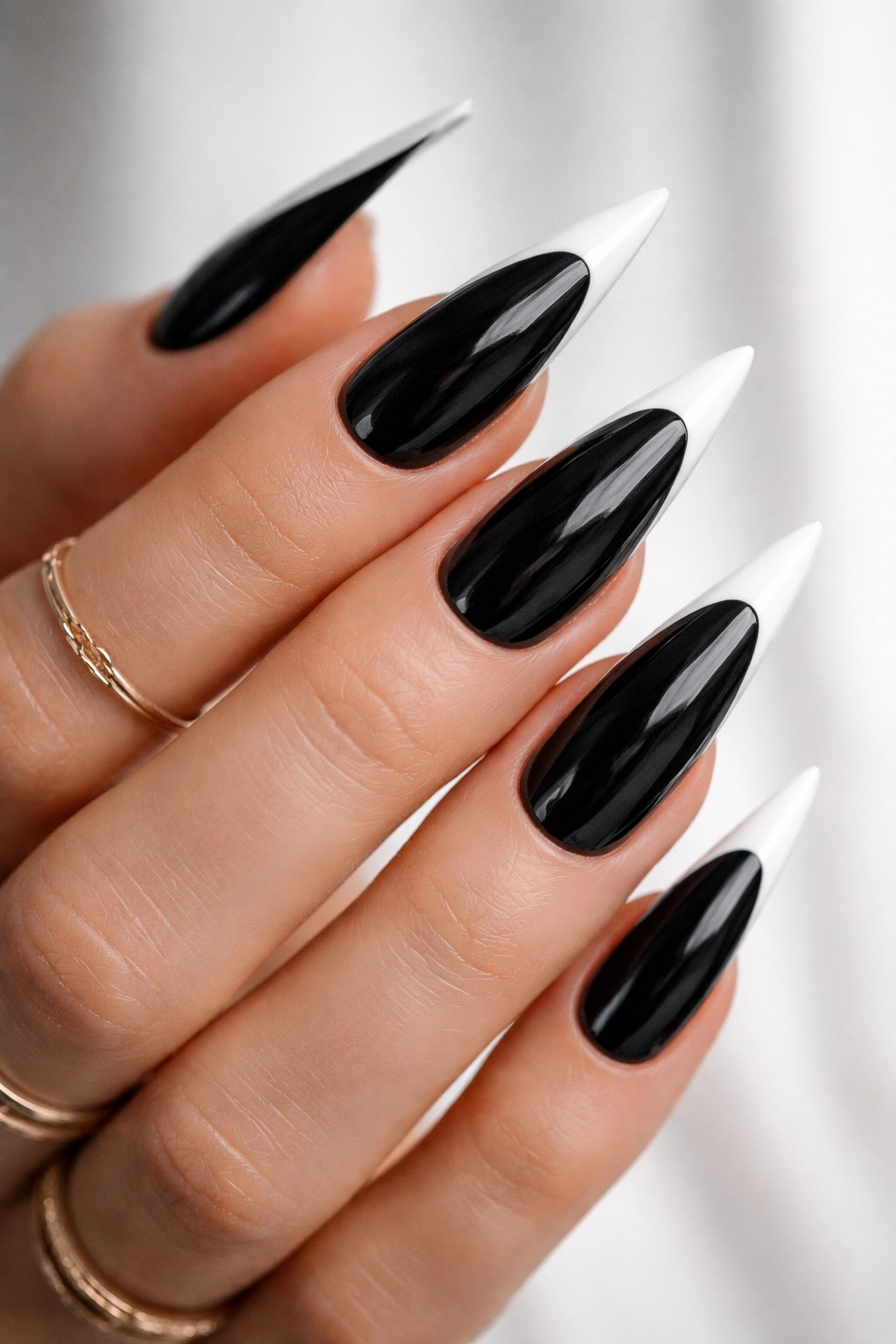 Close-up of black stiletto nails with white reversed tips on a clean background