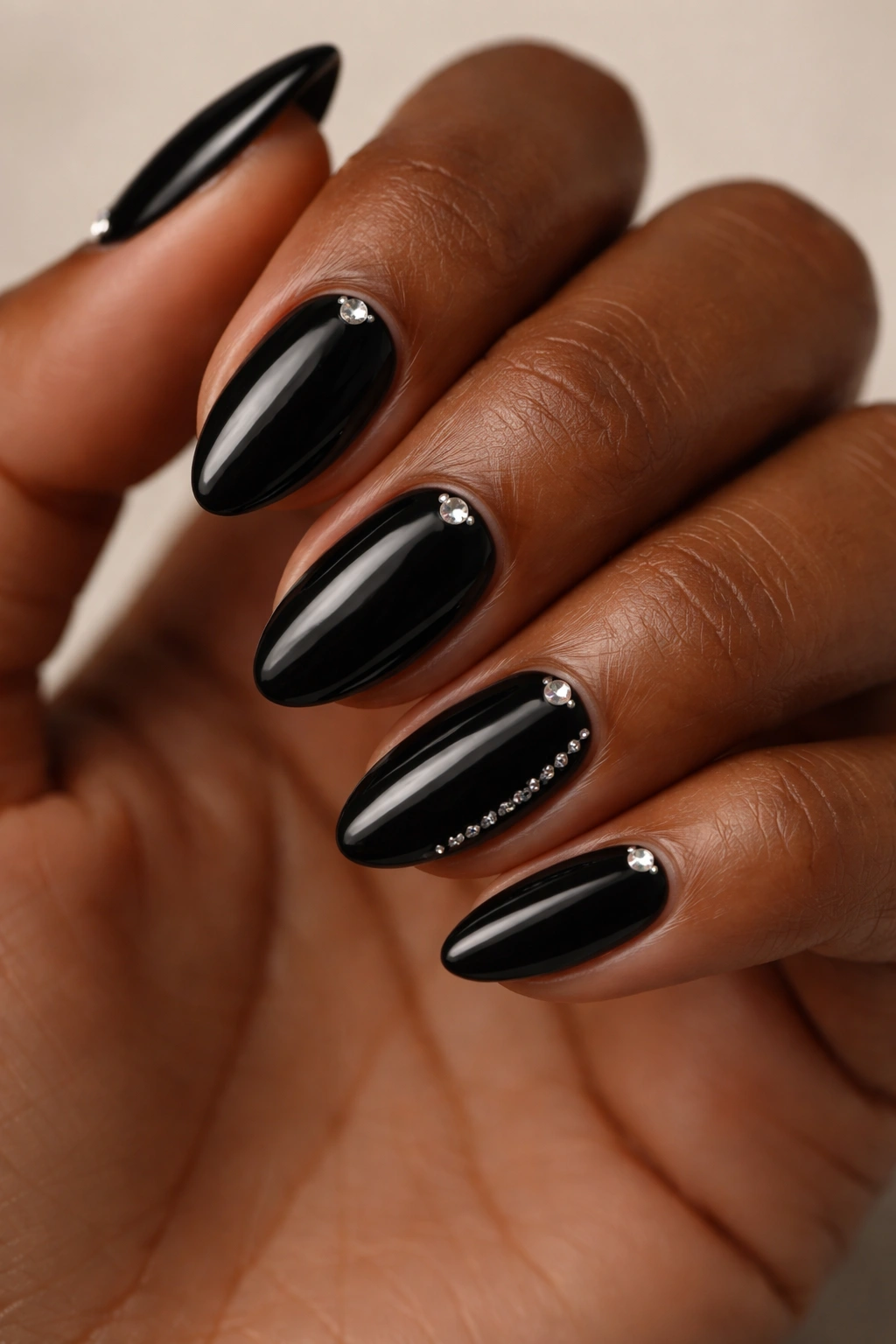 Close-up of black almond nails with tiny rhinestones near the cuticle on dark skin