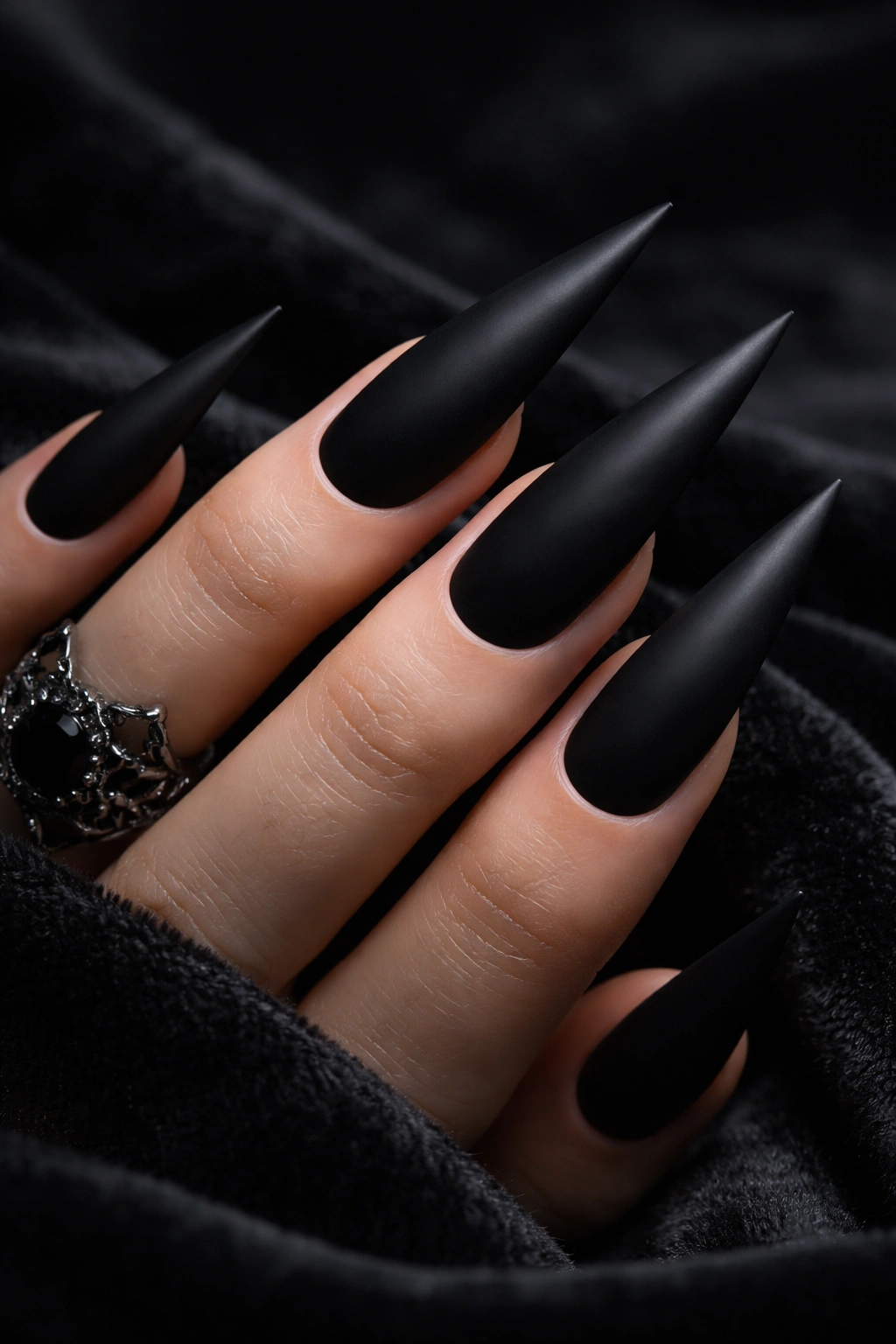 Close-up of jet-black matte stiletto nails on a hand with dark background