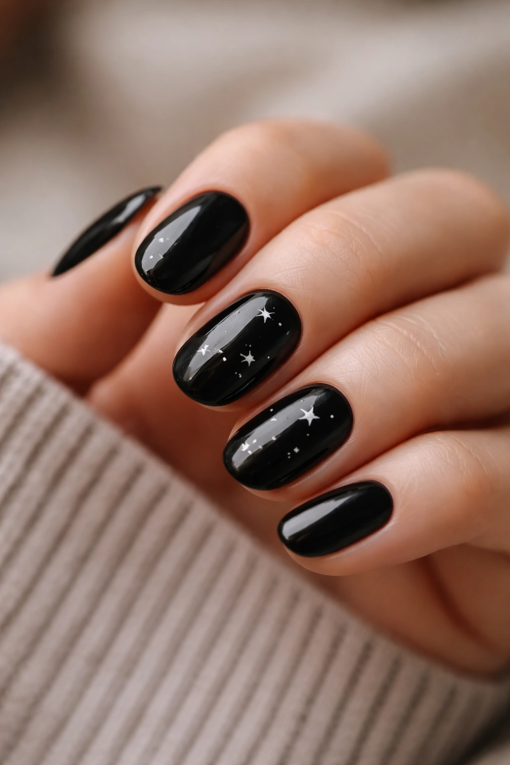 Close-up of short oval black nails with tiny white star accents