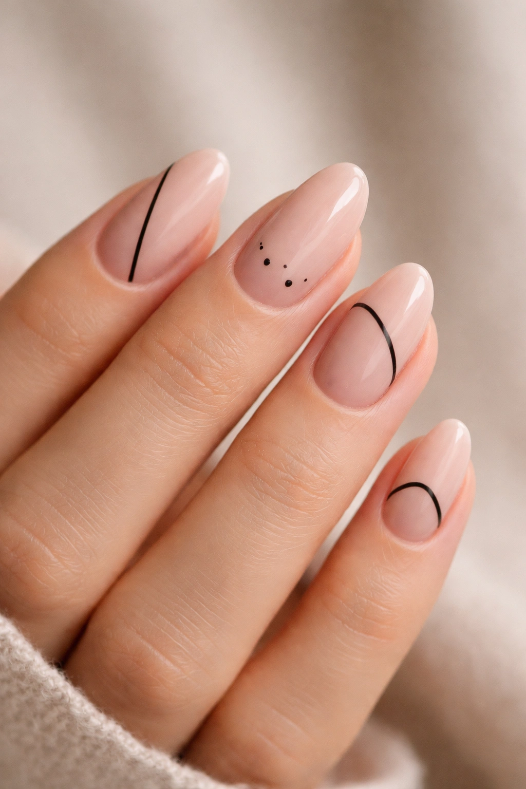 Close-up of short almond nails with nude base and delicate black line art.