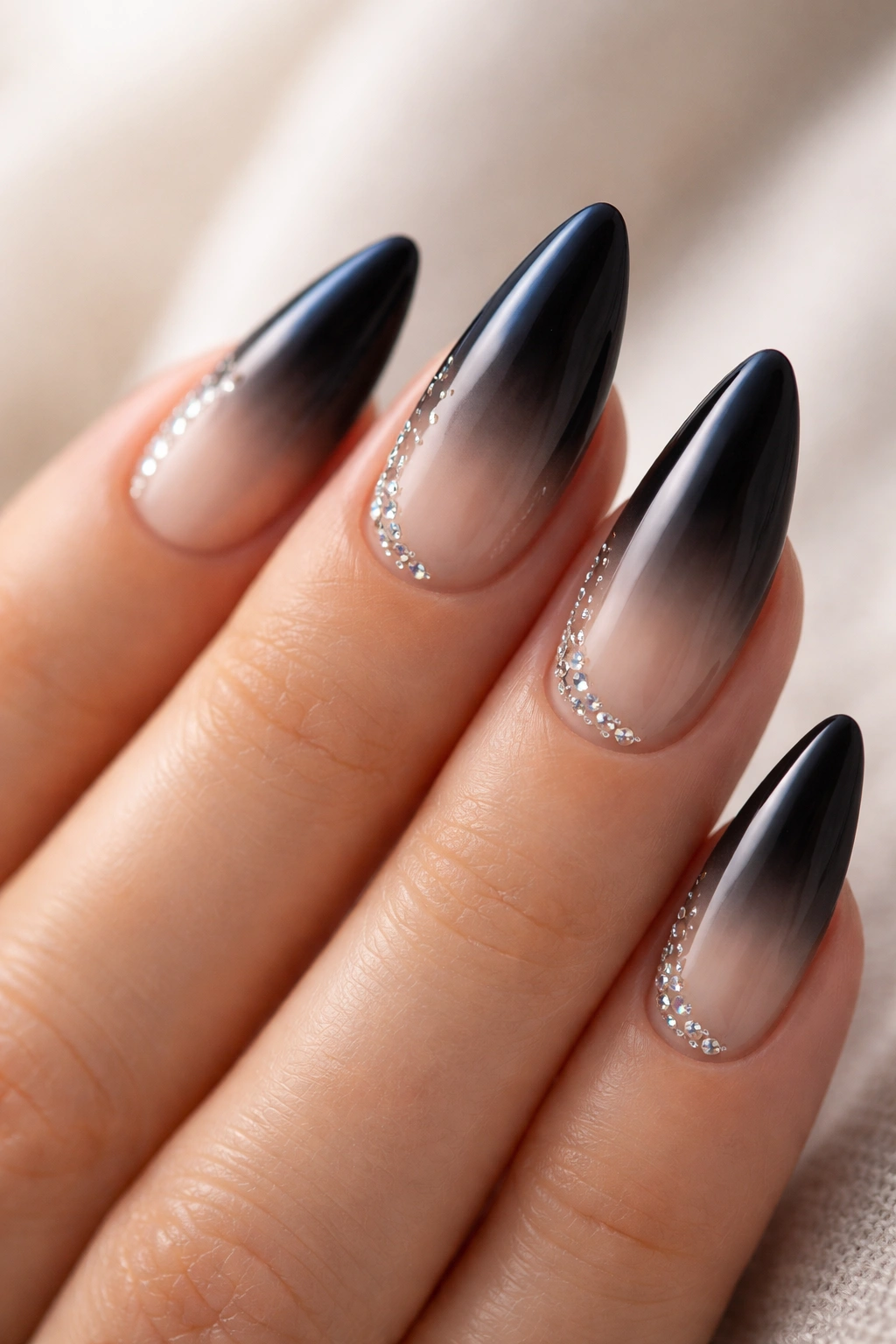 Close-up of almond nails with black ombre and sparse rhinestones on a neutral background