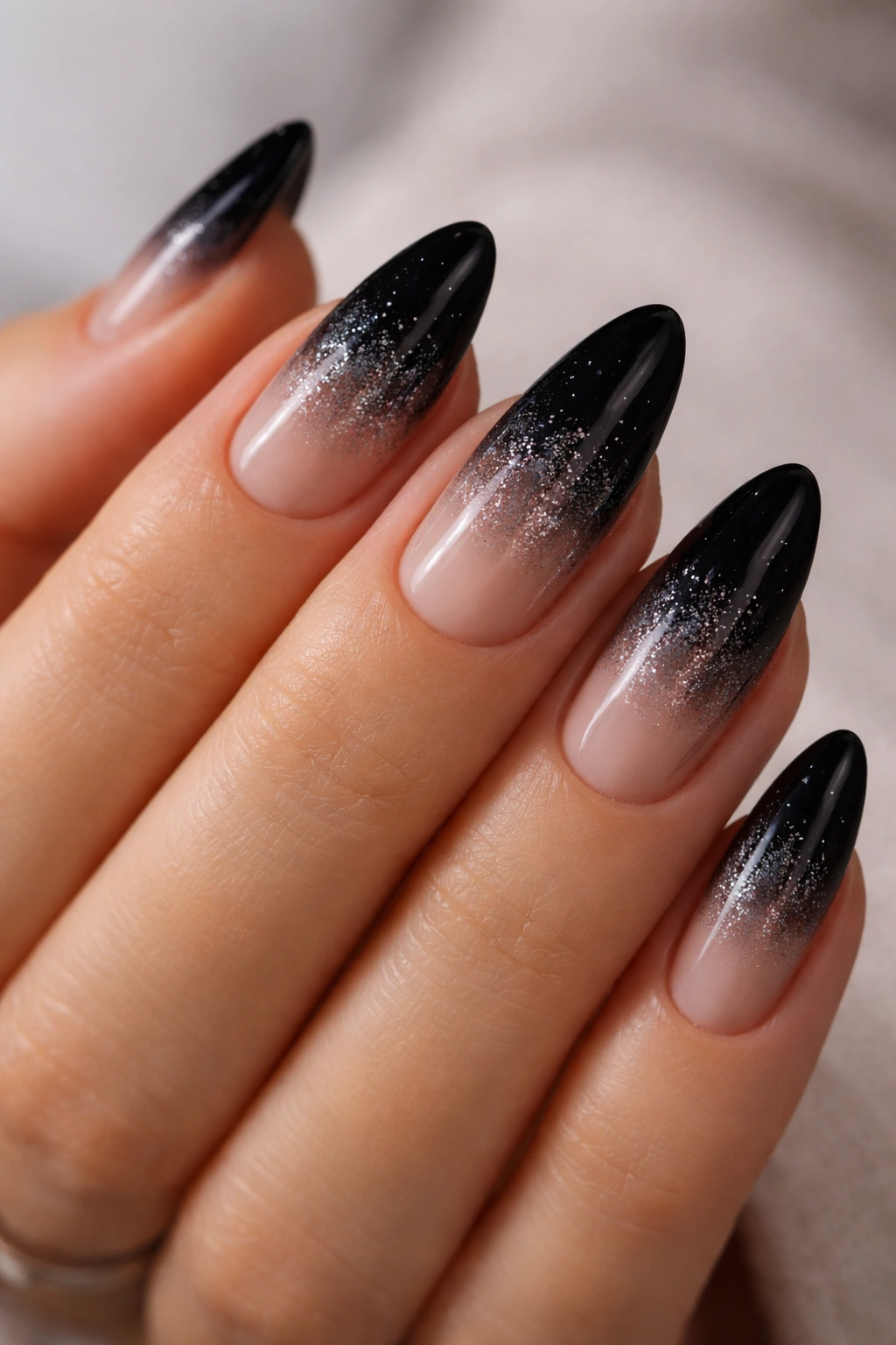 Close-up of almond nails with black ombre and tiny silver glitter at transition