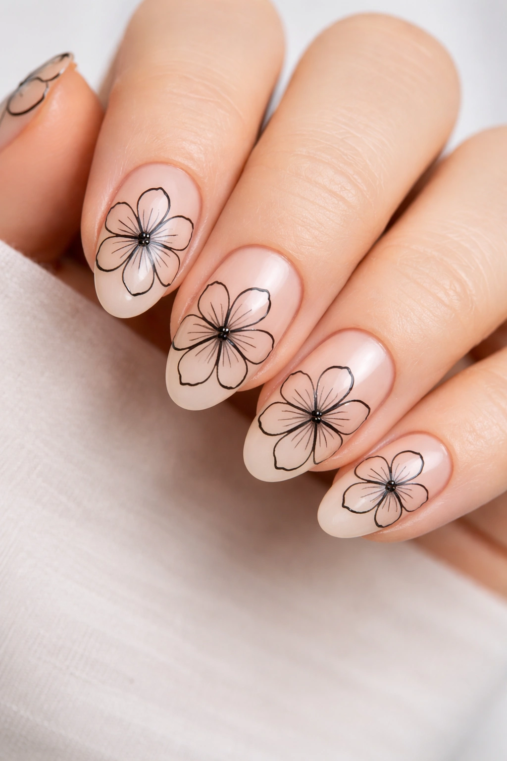 Close-up of black outline floral nail art on short almond nails with a sheer base.