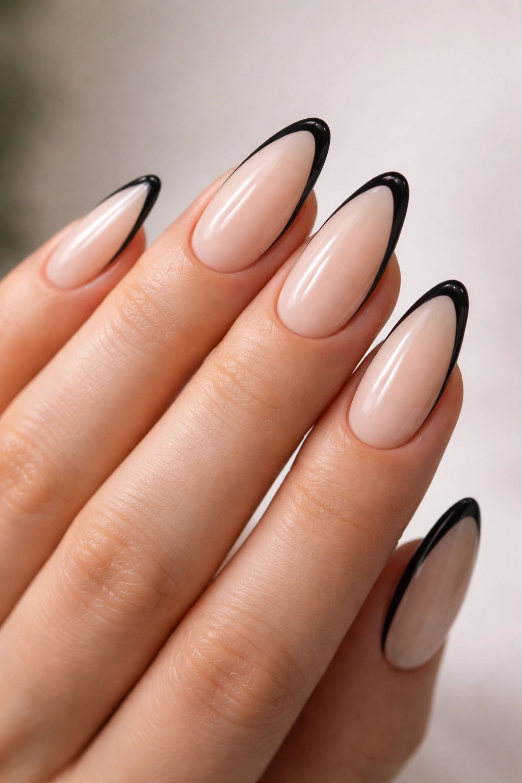 Almond nails with a thin black outline along the French tip on a nude base.