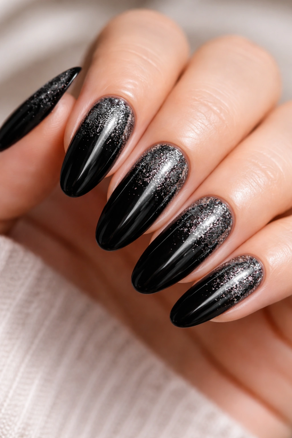 Close-up of long black oval nails with silver glitter fade near the tips
