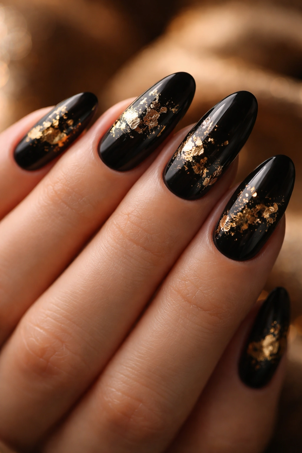 Close-up of black oval nails with gold foil accents