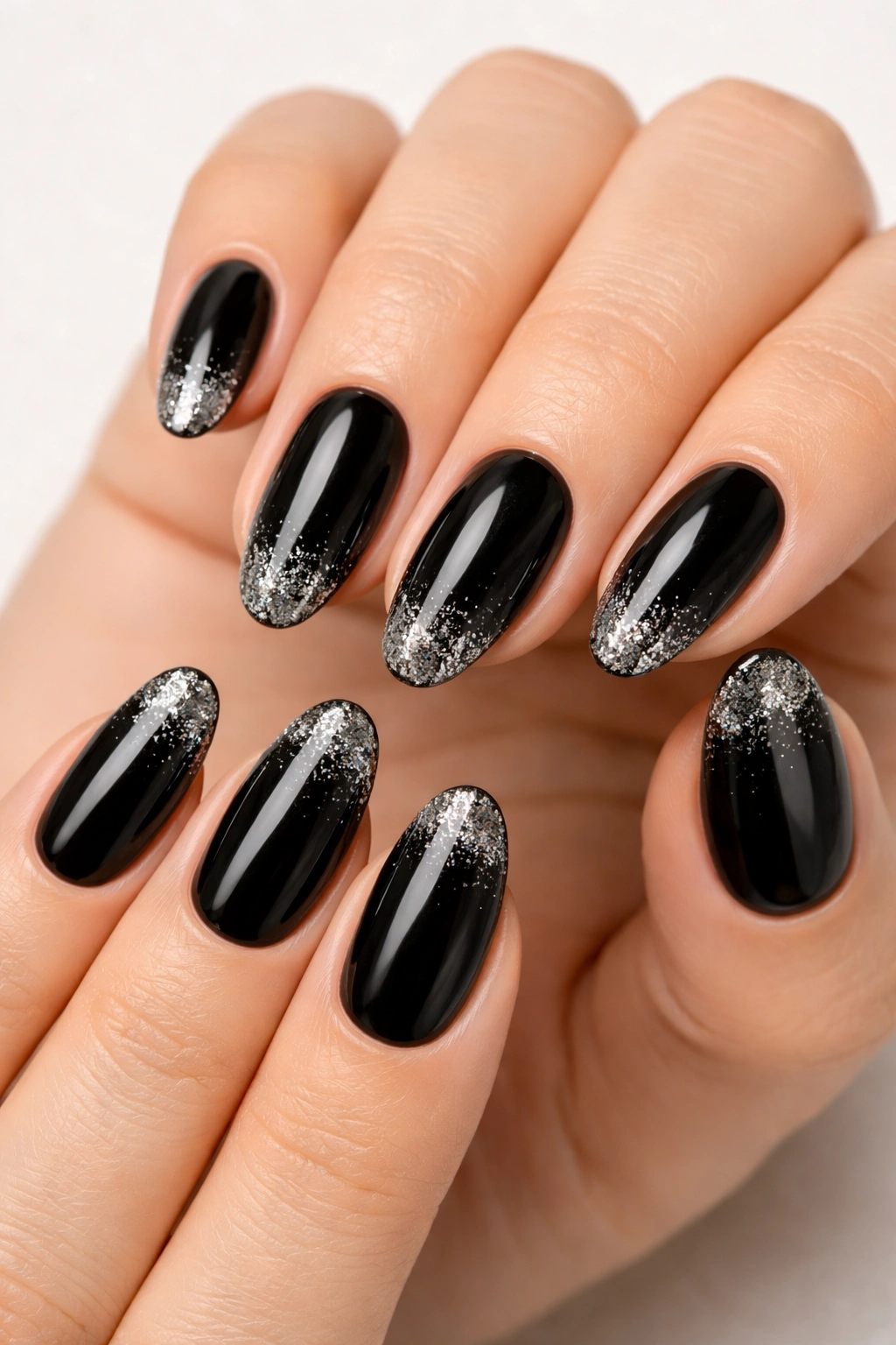 Close-up of black oval nails with silver glitter at the tips