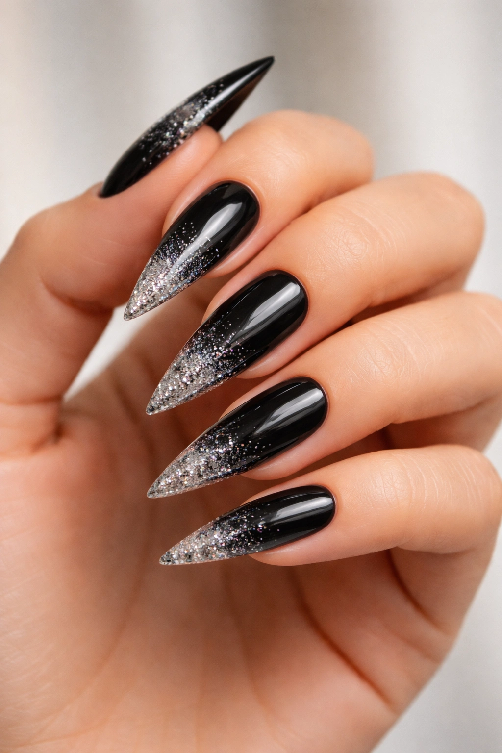 Close-up of black stiletto nails with glitter gradient at tips