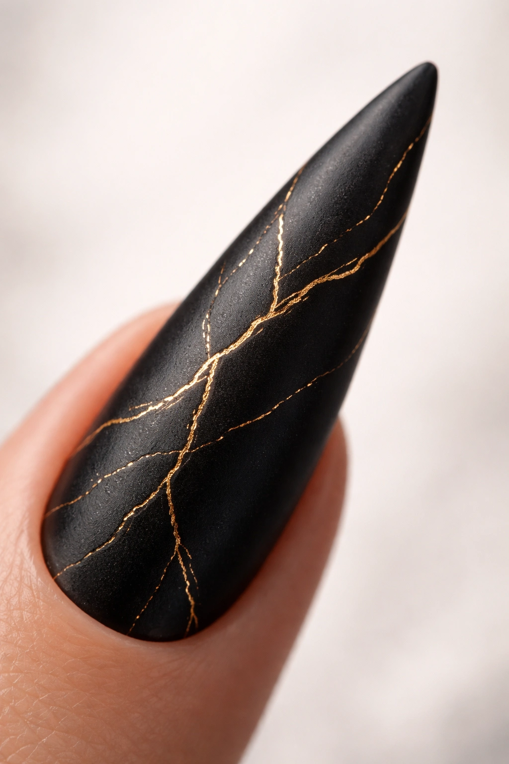 Close-up of matte black stiletto nail with gold veining