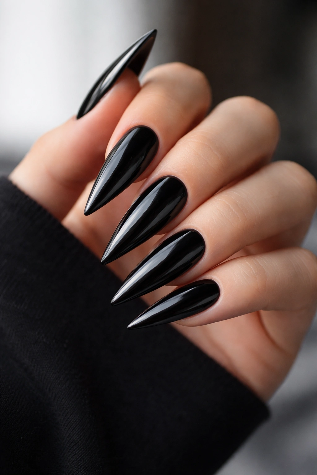 Close-up of glossy black stiletto nails on a hand with mirror-like finish