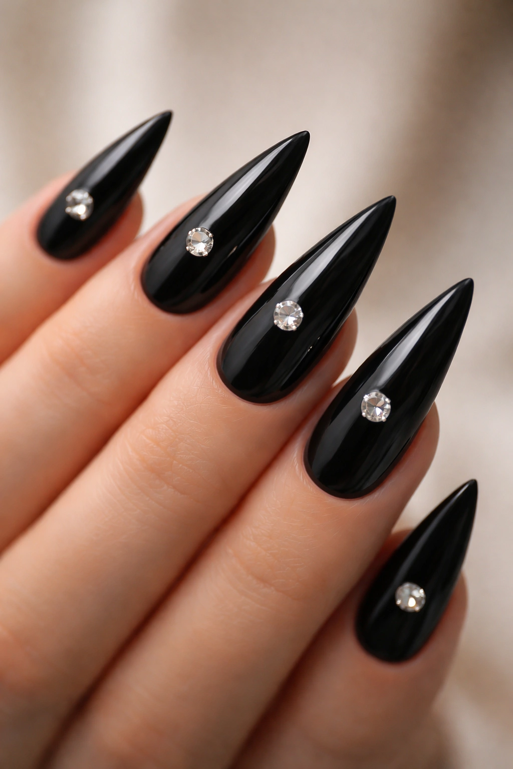 Close-up of black stiletto nails with a single centered rhinestone on each nail