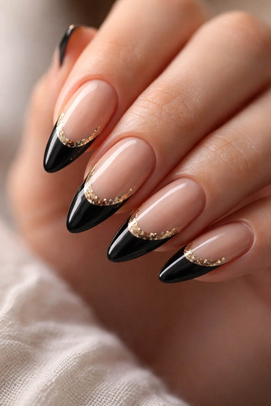 Almond nails with black tips and gold foil accents on a nude base.