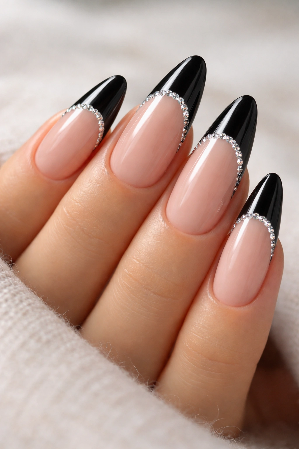 Close-up of long almond nails with black tips and a row of tiny rhinestones along the smile line.