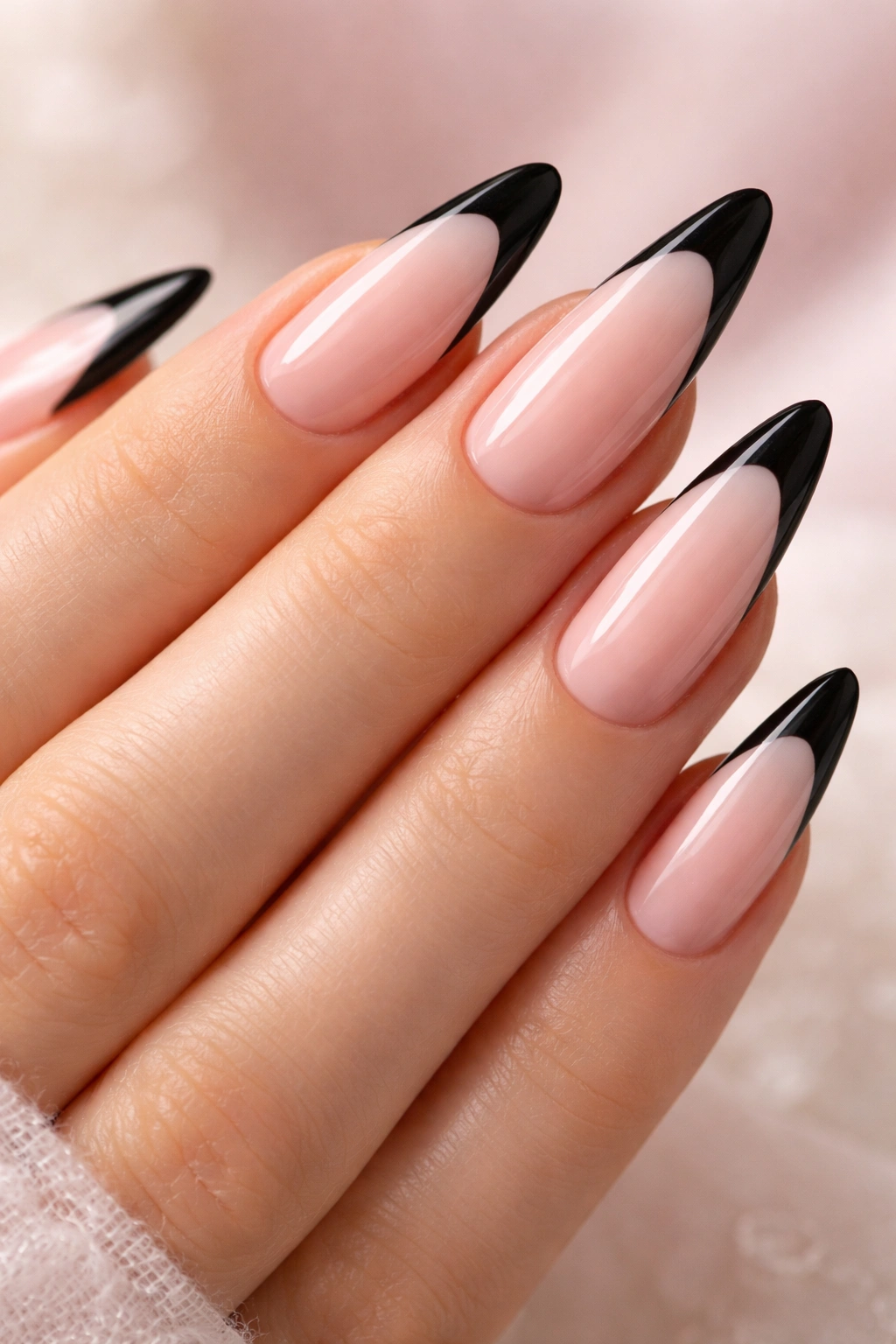 Close-up of long almond nails with black tips on a soft pink base.