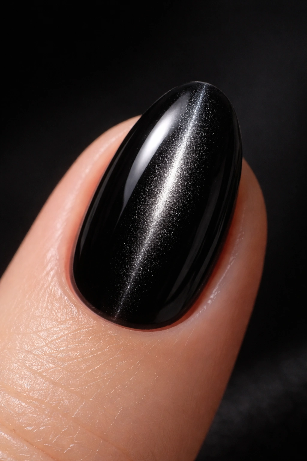 Close-up of a short almond nail in black with a narrow cat-eye shimmer
