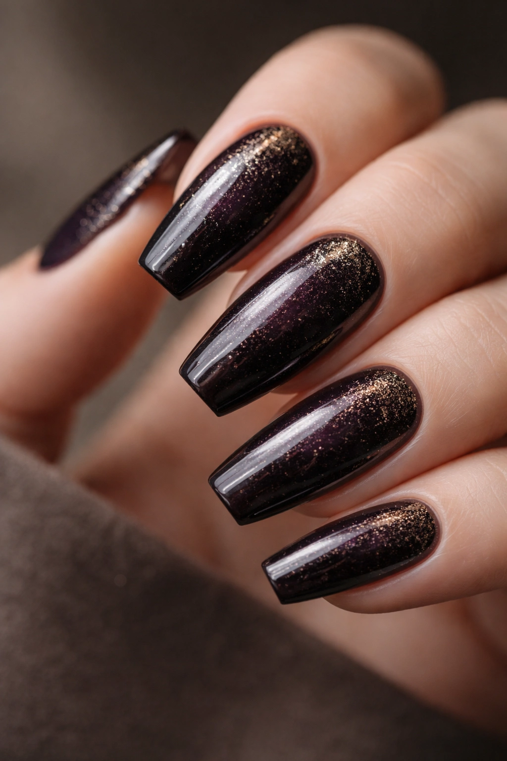 Close-up of medium coffin nails in deep blackened plum with gold dust and glossy topcoat