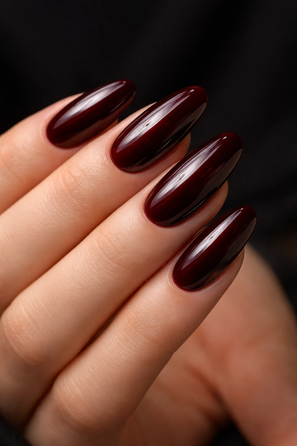 Close-up of blackened red oval nails with glossy finish