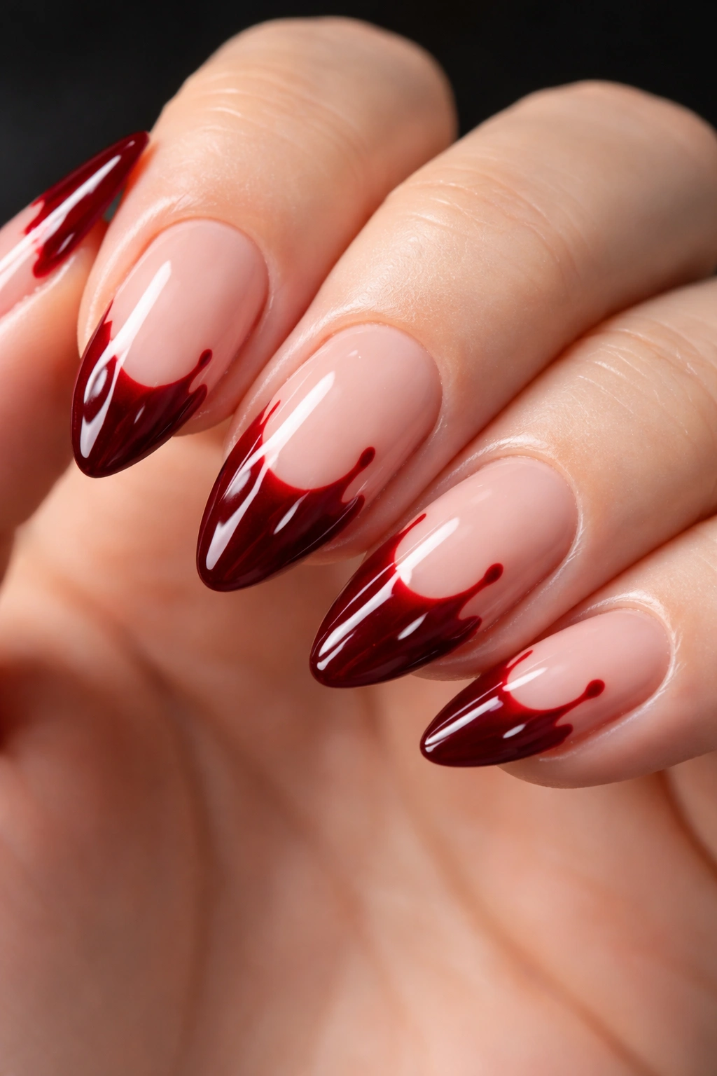 Close-up of a short almond nail with deep blood red vampire drip tips on a nude base