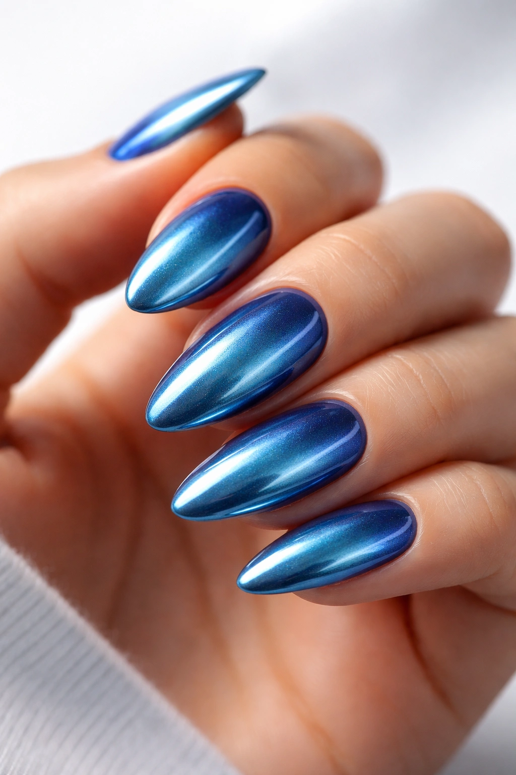 Close-up of blue chrome almond nails catching light