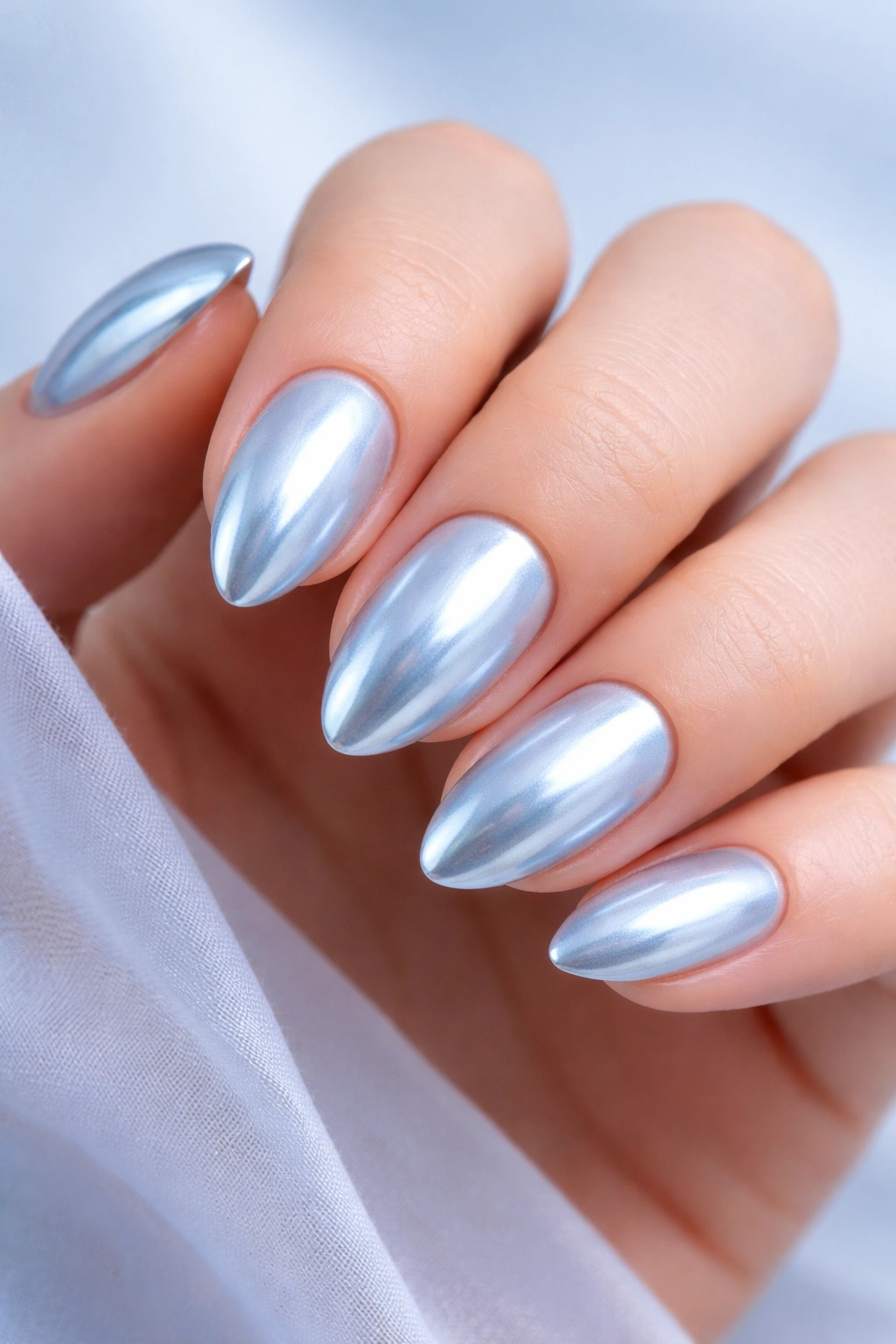Close-up of short almond nails with icy blue chrome finish on pale blue base