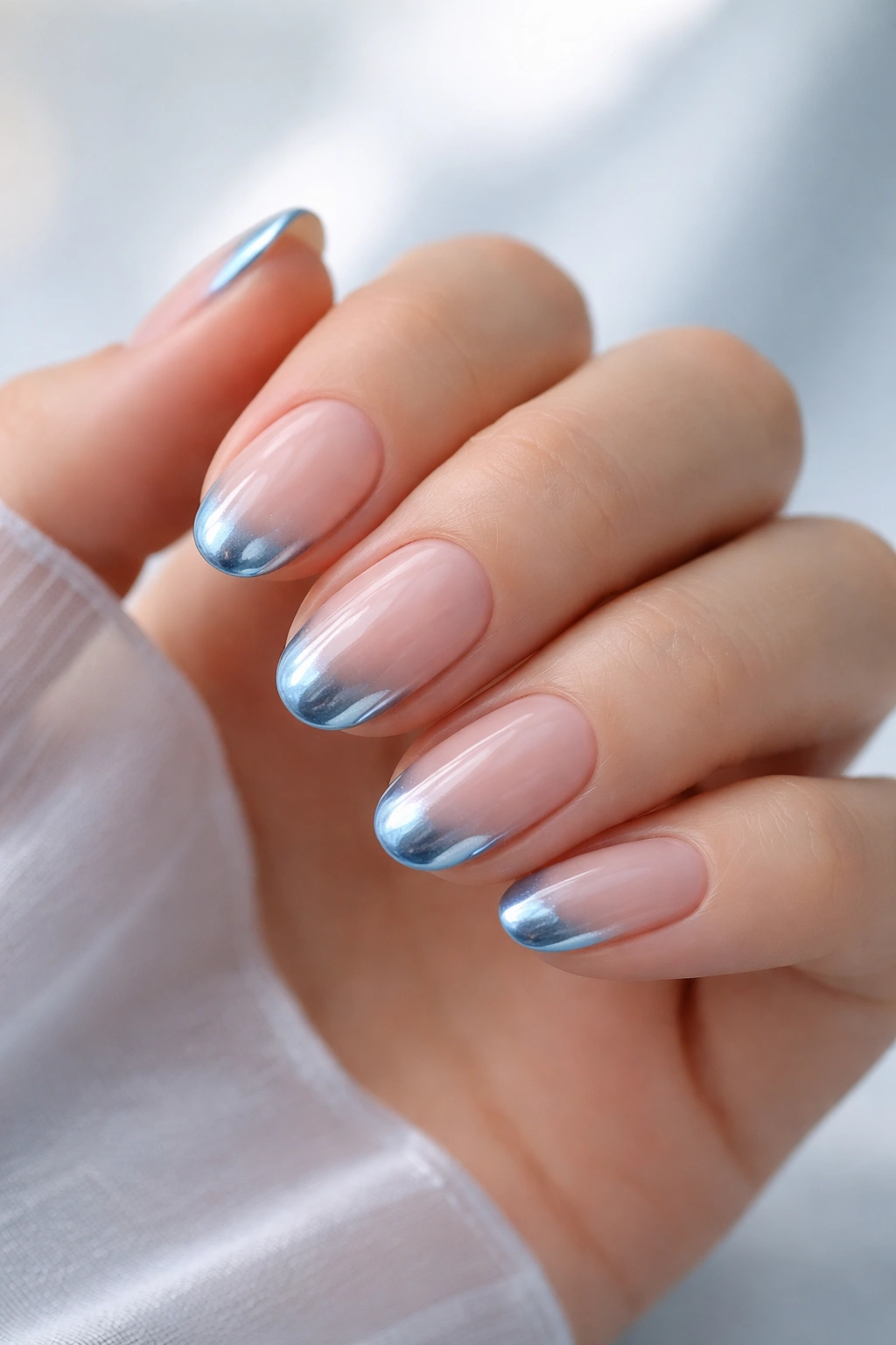 Close-up of short oval nails with icy blue chrome tips on a pale base.