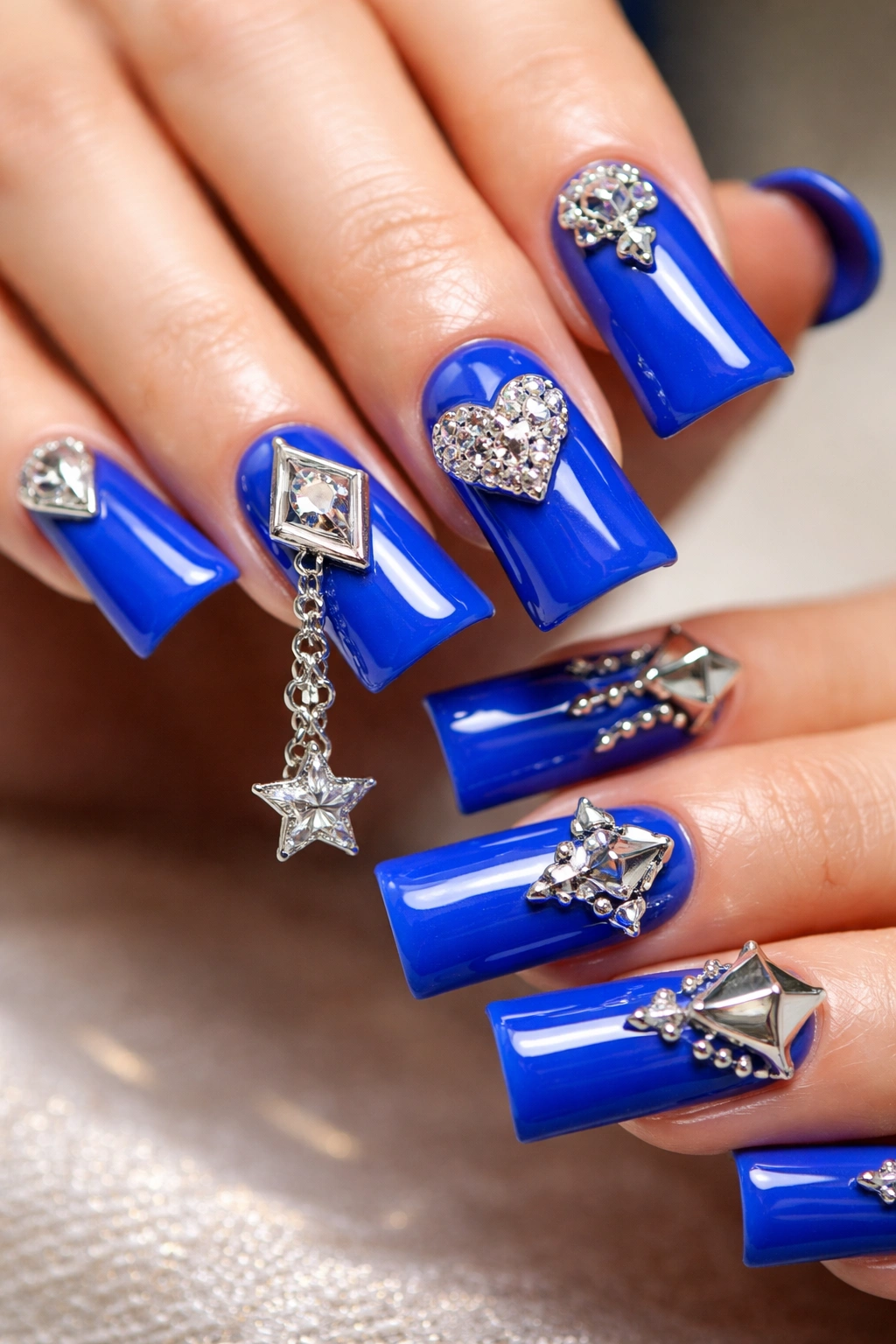 Close-up of blue duck nails with 3D metal charms showing depth and shine