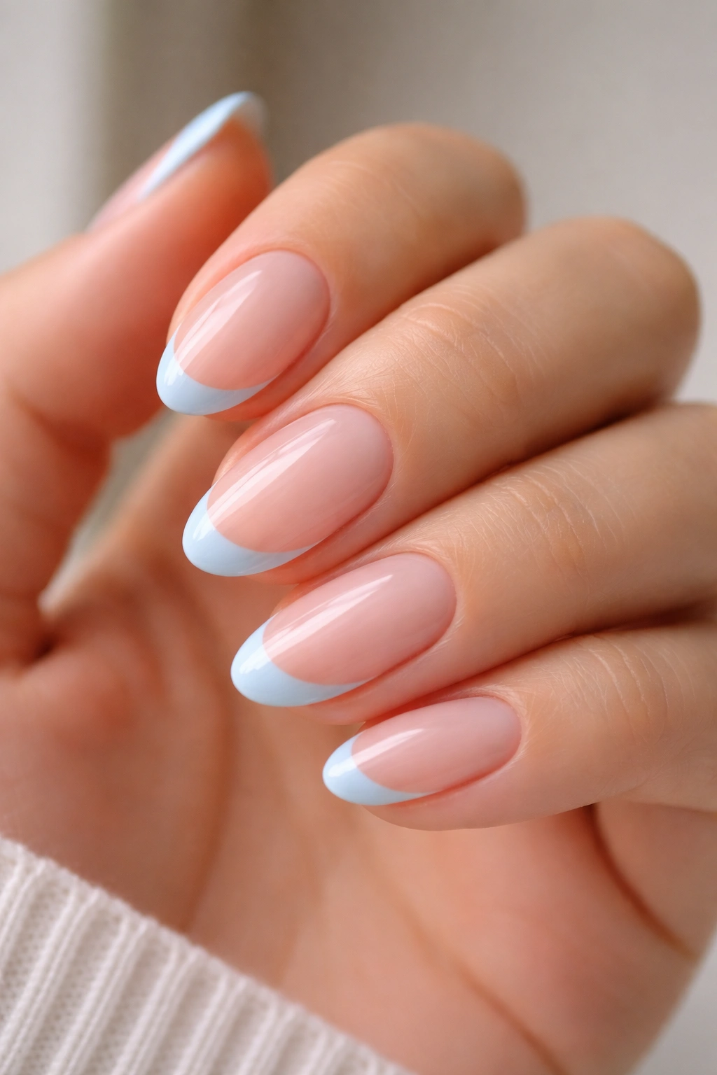 Close-up of short almond nails with sheer pink base and baby blue French tips