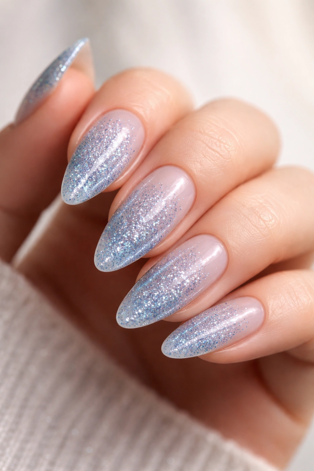 Close-up of blue glitter almond nails over a sheer base