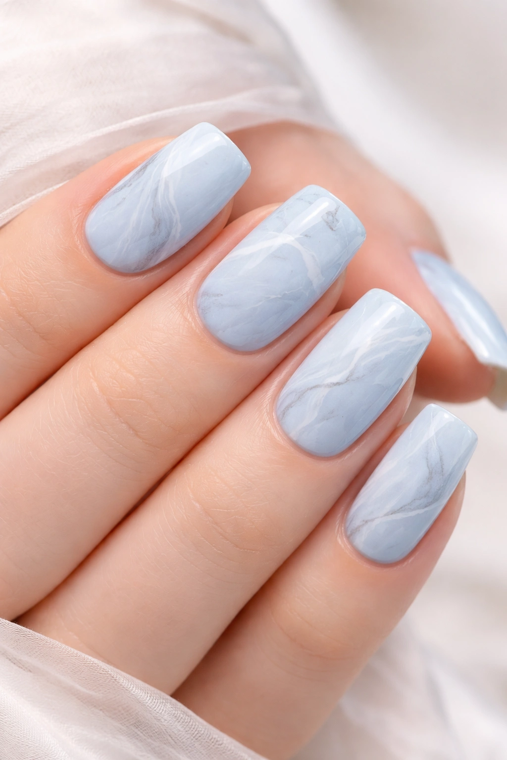 Nails with soft blue marble pattern featuring white and gray veining.