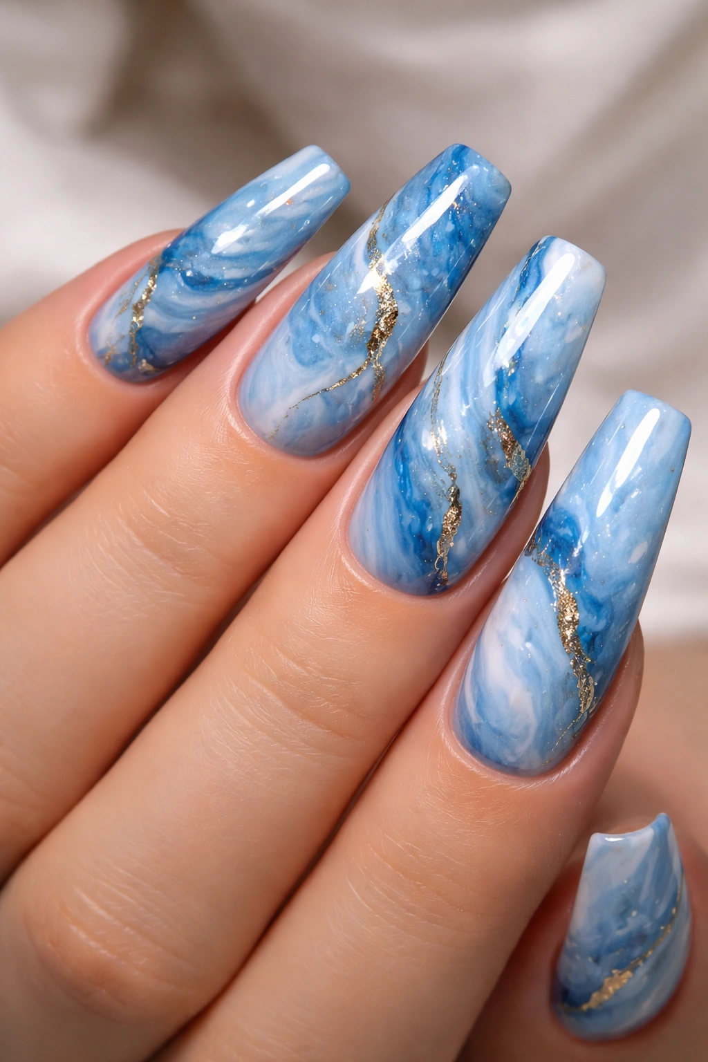 Close-up of blue marble acrylic nails with white veins and glossy finish