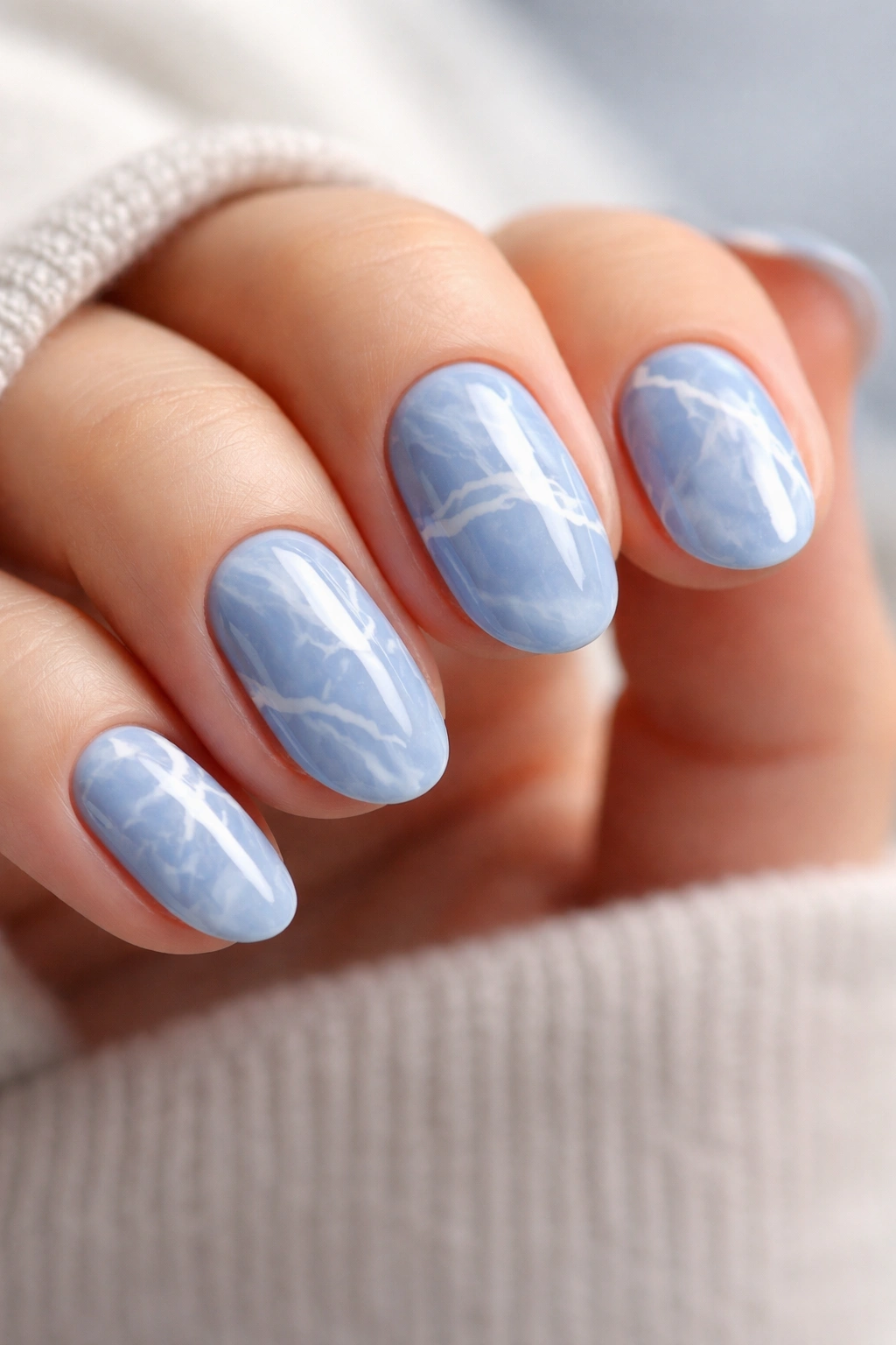 Close-up of blue marble nails with white veining on short oval nails
