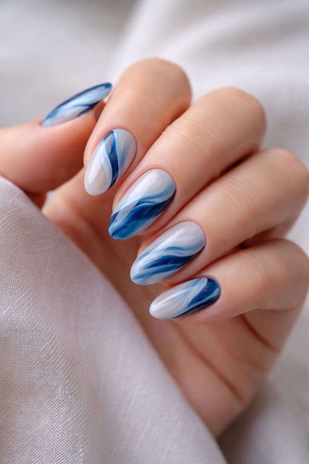 Short almond nails with a loose blue marble swirl pattern.