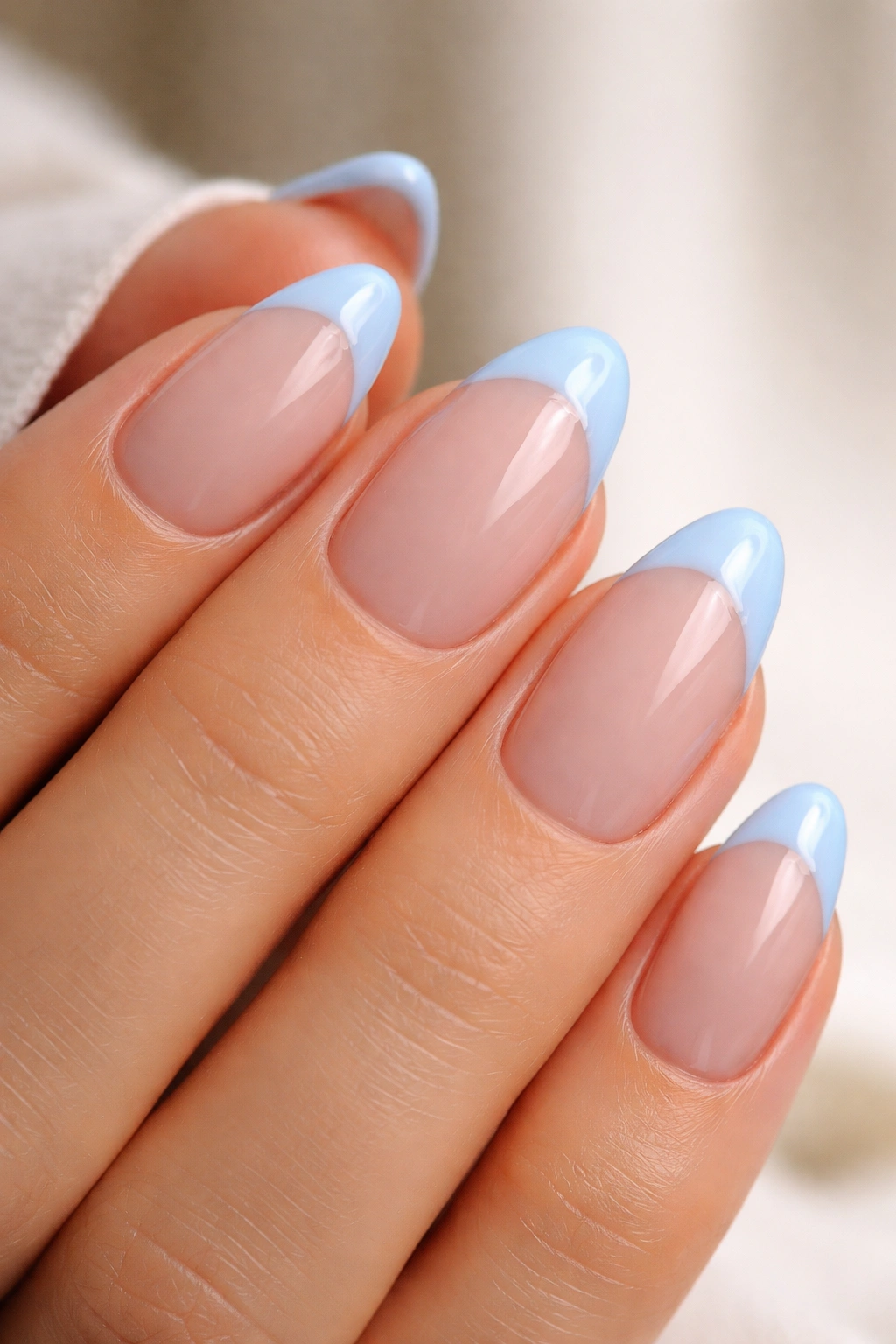 Close-up of almond-shaped nails with blue French tips and glossy top coat highlighting durability and edge sealing