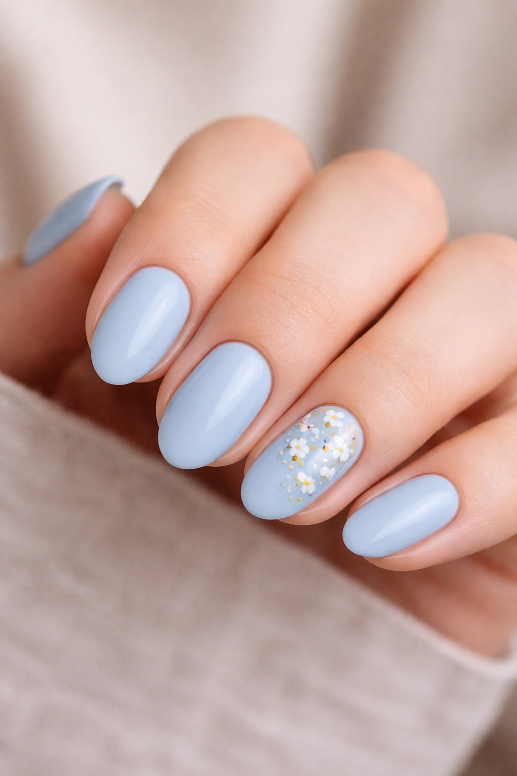 Close-up of short almond nails with blue base and a tiny white floral accent on one nail
