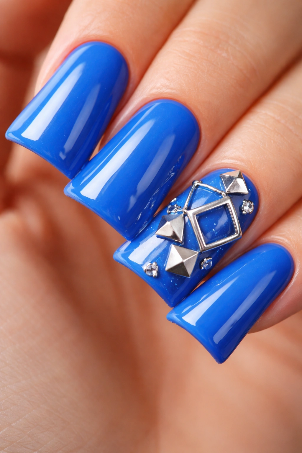 Blue nails with silver geometric charms on an accent nail, macro shot