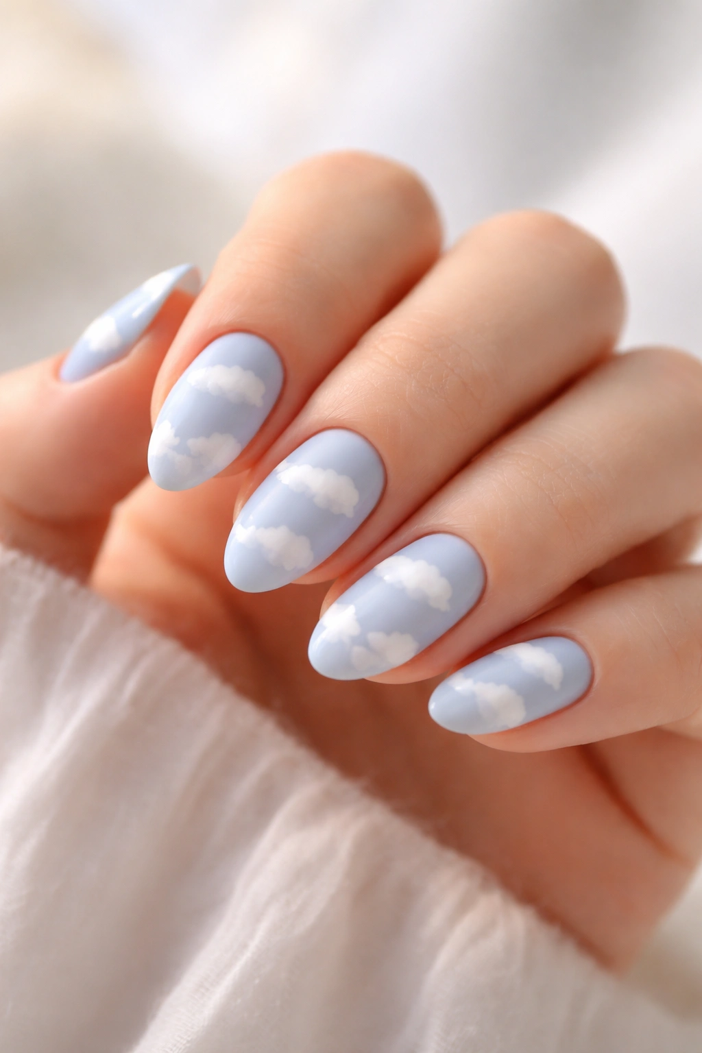 Close-up of baby blue nails with white cloud art on short almond nails