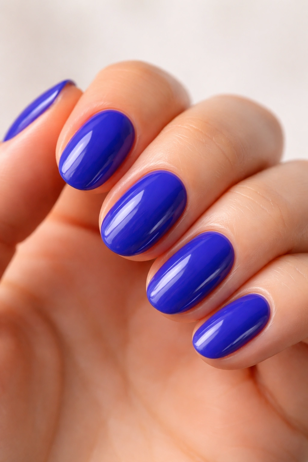 Close-up of a blue raspberry short oval nail with glossy finish on neutral background